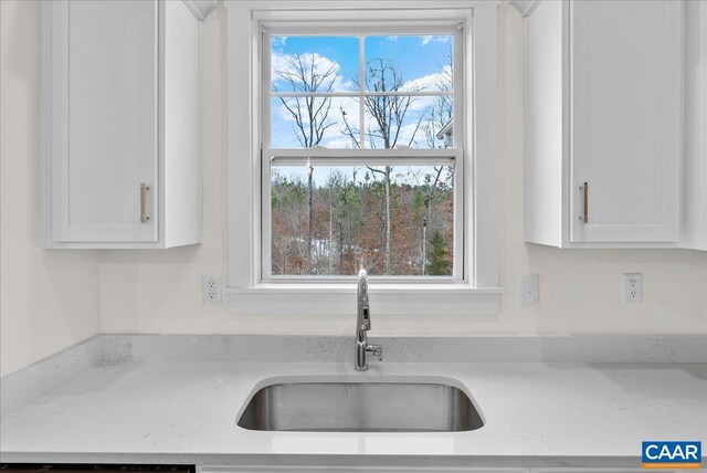 kitchen with a healthy amount of sunlight, sink, white cabinets, and light stone counters