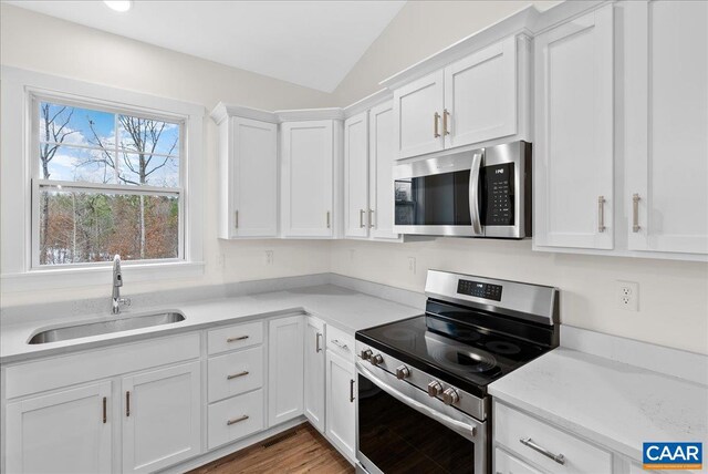 kitchen with sink, appliances with stainless steel finishes, hardwood / wood-style floors, white cabinets, and vaulted ceiling