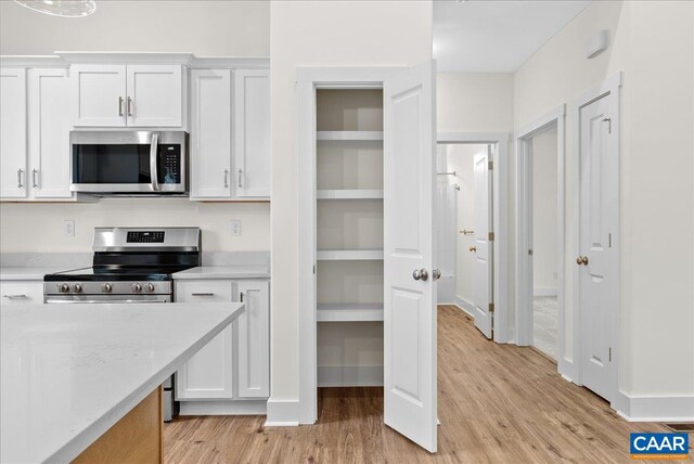 kitchen with light stone countertops, light hardwood / wood-style flooring, stainless steel appliances, and white cabinets