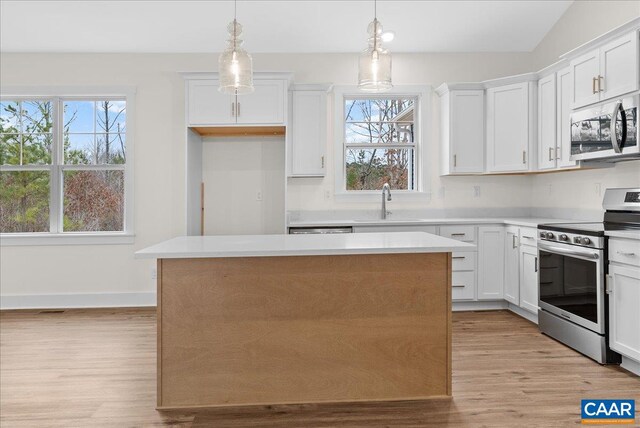 kitchen featuring appliances with stainless steel finishes, a center island, light hardwood / wood-style floors, white cabinets, and decorative light fixtures