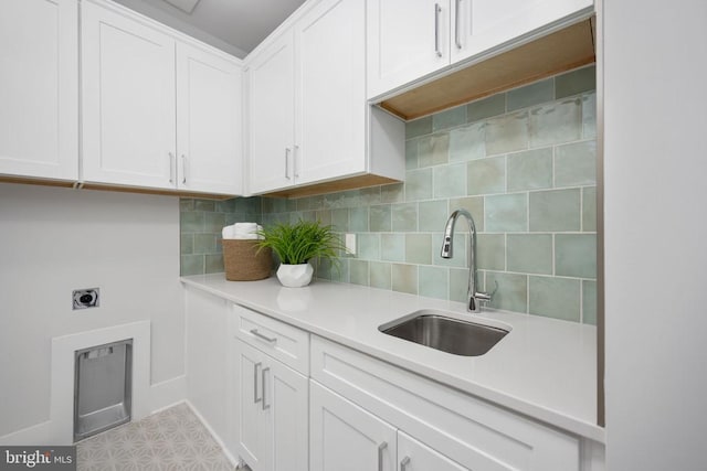 kitchen with light countertops, backsplash, a sink, and white cabinetry