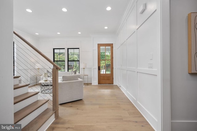 foyer featuring light wood-style flooring, recessed lighting, a decorative wall, ornamental molding, and stairway