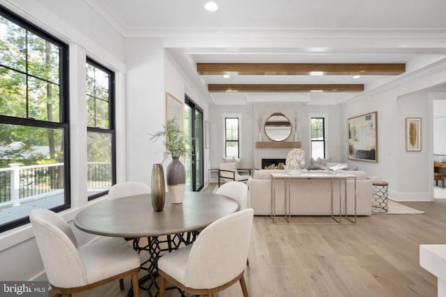 dining space with light wood-type flooring, a warm lit fireplace, baseboards, and beam ceiling