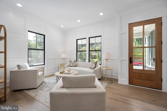 living area featuring crown molding, recessed lighting, light wood-type flooring, and a decorative wall