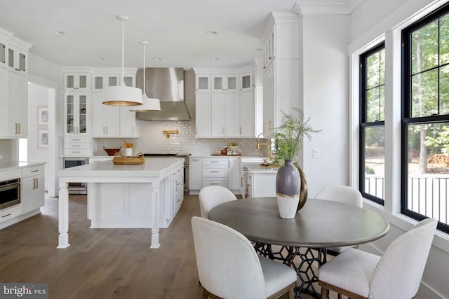 kitchen featuring wall chimney exhaust hood, a kitchen island, glass insert cabinets, and light countertops