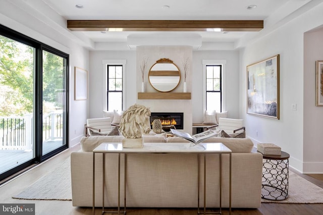 living area with a fireplace, baseboards, beam ceiling, and wood finished floors