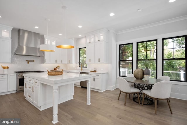 kitchen featuring wall chimney exhaust hood, appliances with stainless steel finishes, glass insert cabinets, and light countertops