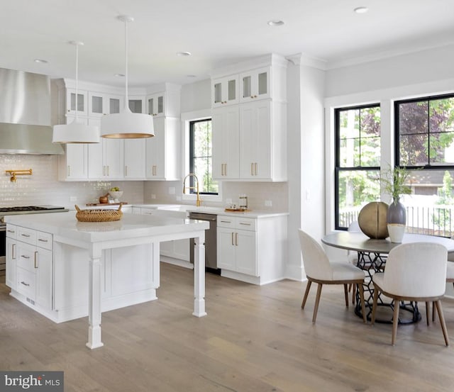 kitchen featuring glass insert cabinets, wall chimney range hood, appliances with stainless steel finishes, and light countertops