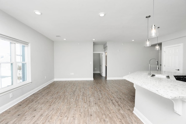 kitchen featuring light stone counters, decorative light fixtures, light wood finished floors, a sink, and baseboards