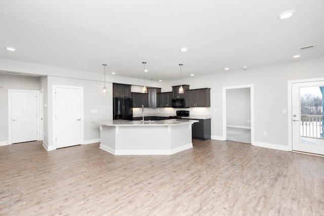 kitchen with hardwood / wood-style floors, decorative light fixtures, black appliances, and a center island with sink