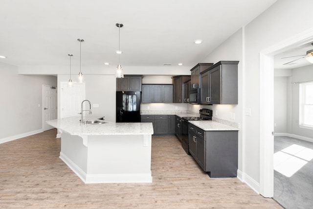 kitchen with sink, light hardwood / wood-style floors, black appliances, an island with sink, and decorative light fixtures