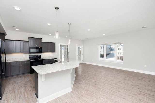 kitchen with a sink, light wood-style floors, hanging light fixtures, black appliances, and a center island with sink