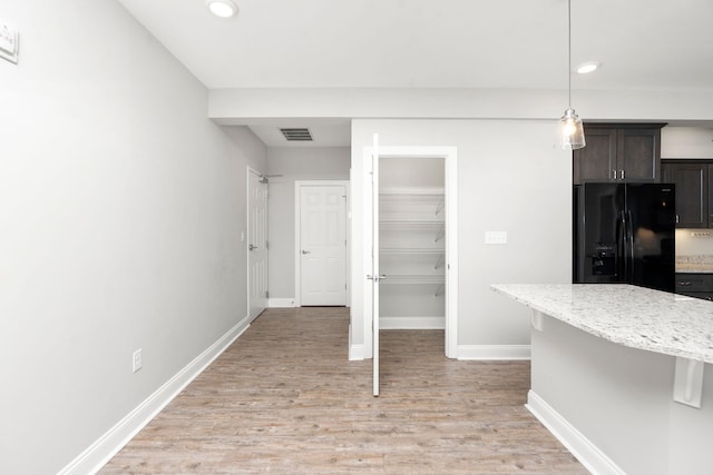 kitchen featuring light stone counters, decorative light fixtures, black refrigerator with ice dispenser, dark brown cabinets, and light hardwood / wood-style floors