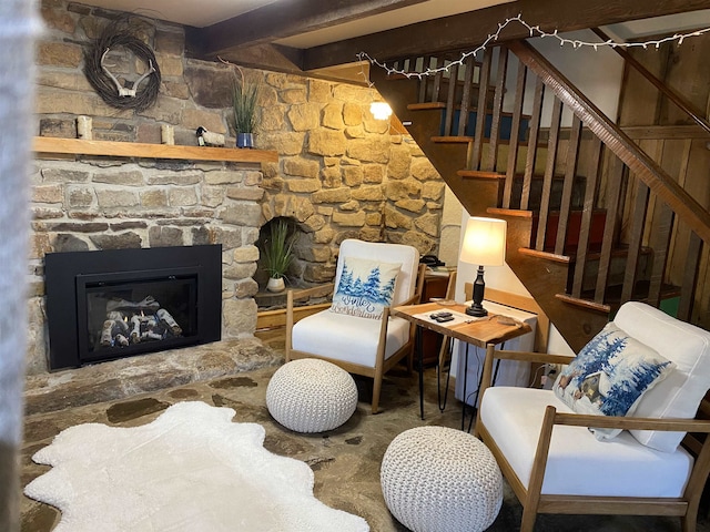 living area featuring stairway, beamed ceiling, and a stone fireplace