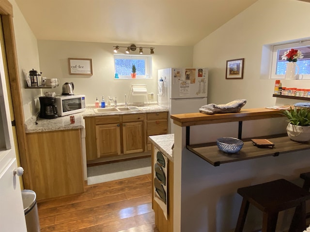 kitchen with light countertops, light wood-style floors, a sink, vaulted ceiling, and white appliances