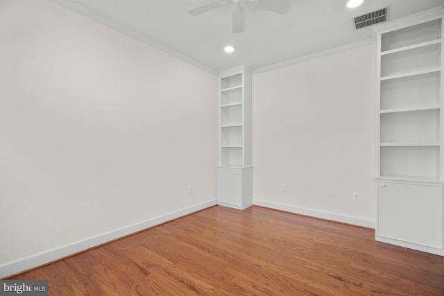 spare room featuring visible vents, baseboards, built in features, ornamental molding, and wood finished floors