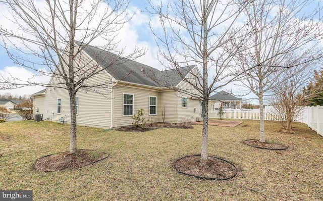 back of house featuring a lawn, central AC, a shingled roof, and fence