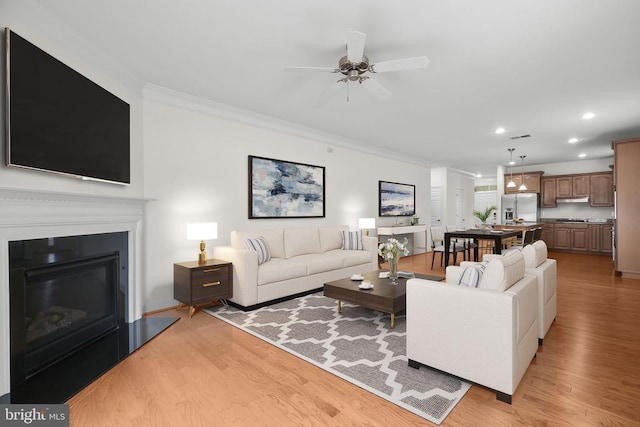 living room featuring recessed lighting, a glass covered fireplace, light wood-style flooring, and crown molding