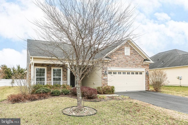 view of front of home featuring a front yard, covered porch, a garage, stone siding, and aphalt driveway