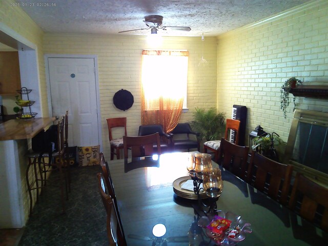 dining room featuring ceiling fan, brick wall, and a textured ceiling