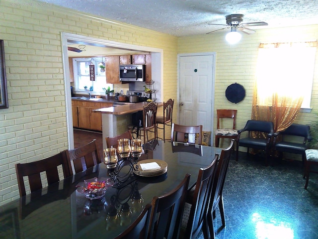 dining area featuring ceiling fan, brick wall, sink, and a textured ceiling