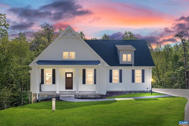 view of front of home with a yard, a porch, and a shingled roof