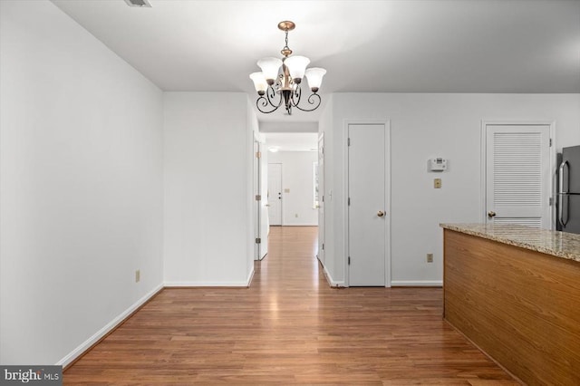 unfurnished dining area featuring a notable chandelier, light wood-type flooring, and baseboards