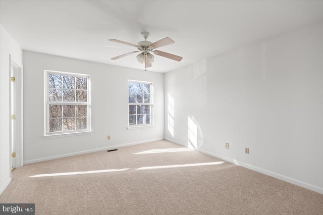 carpeted spare room with baseboards, visible vents, and ceiling fan