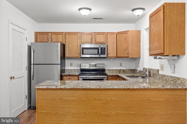 kitchen featuring visible vents, a sink, stainless steel appliances, a peninsula, and light stone countertops