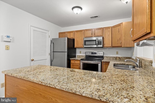 kitchen with visible vents, light stone countertops, brown cabinetry, stainless steel appliances, and a sink