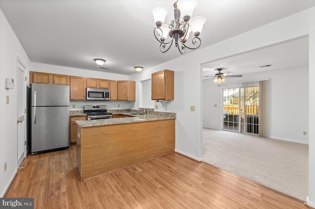 kitchen featuring brown cabinetry, light wood finished floors, a peninsula, a sink, and appliances with stainless steel finishes