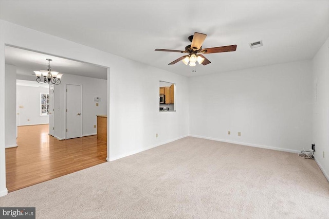 spare room featuring visible vents, baseboards, light carpet, ceiling fan with notable chandelier, and light wood-style floors