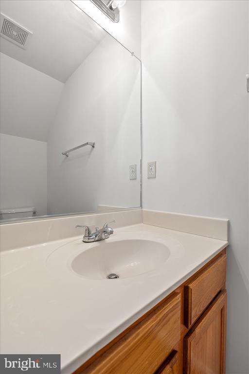 bathroom with visible vents, toilet, vanity, and vaulted ceiling