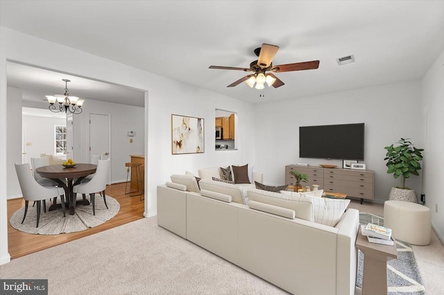 living area with visible vents, ceiling fan with notable chandelier, carpet floors, and wood finished floors