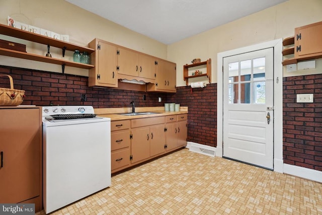 kitchen with open shelves, a sink, washer / clothes dryer, brick wall, and light countertops