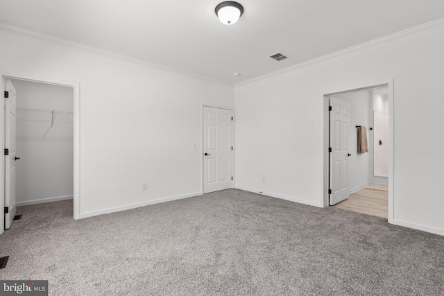 unfurnished bedroom featuring carpet flooring, a walk in closet, visible vents, baseboards, and ornamental molding