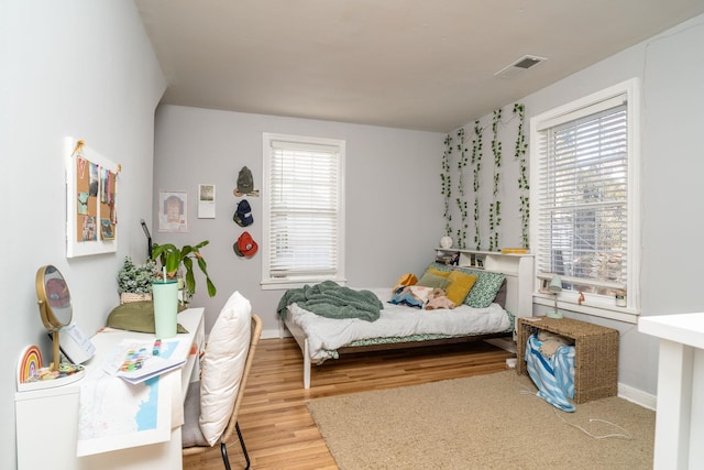 bedroom with multiple windows, wood finished floors, visible vents, and baseboards