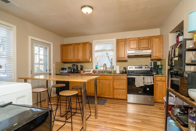 kitchen with stainless steel electric range oven, visible vents, light wood-style flooring, decorative backsplash, and under cabinet range hood