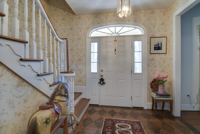foyer entrance with wallpapered walls, an inviting chandelier, and stairway