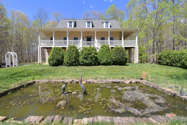 back of property with a small pond, roof with shingles, and a lawn