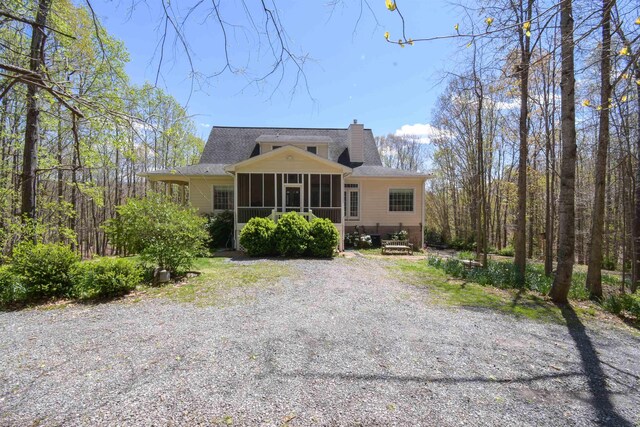 back of house with a shingled roof, a chimney, and a sunroom