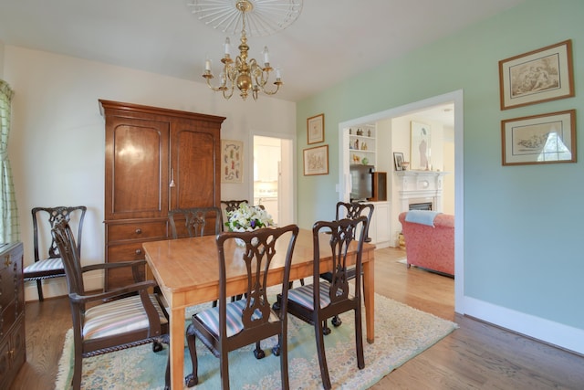 dining room with light wood-style flooring, baseboards, an inviting chandelier, and a fireplace
