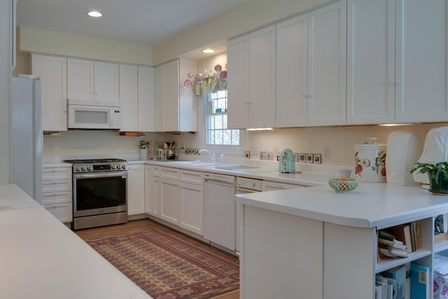 kitchen with white cabinets, a peninsula, white appliances, and light countertops