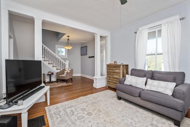 living area with baseboards, decorative columns, wood finished floors, and stairway