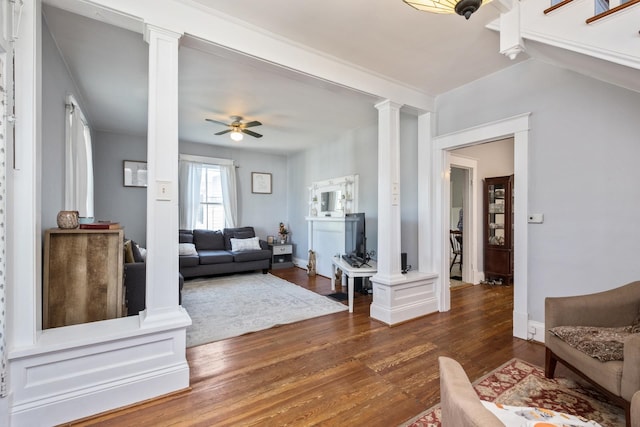 living room featuring ornate columns, baseboards, ceiling fan, and dark wood-style floors