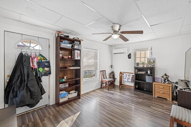 misc room featuring a paneled ceiling, dark hardwood / wood-style floors, a wall mounted AC, and ceiling fan