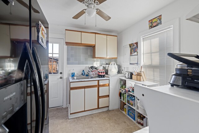 kitchen featuring sink, black fridge, tasteful backsplash, ceiling fan, and white cabinets