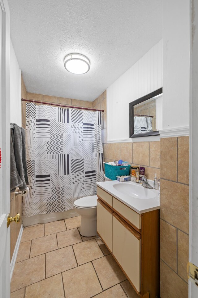 full bathroom featuring tile patterned flooring, tile walls, vanity, a textured ceiling, and toilet