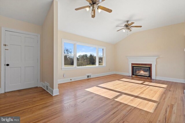 unfurnished living room with visible vents, a brick fireplace, baseboards, lofted ceiling, and wood finished floors