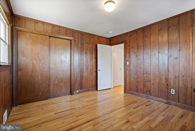 unfurnished bedroom featuring light wood finished floors, visible vents, a closet, and wooden walls